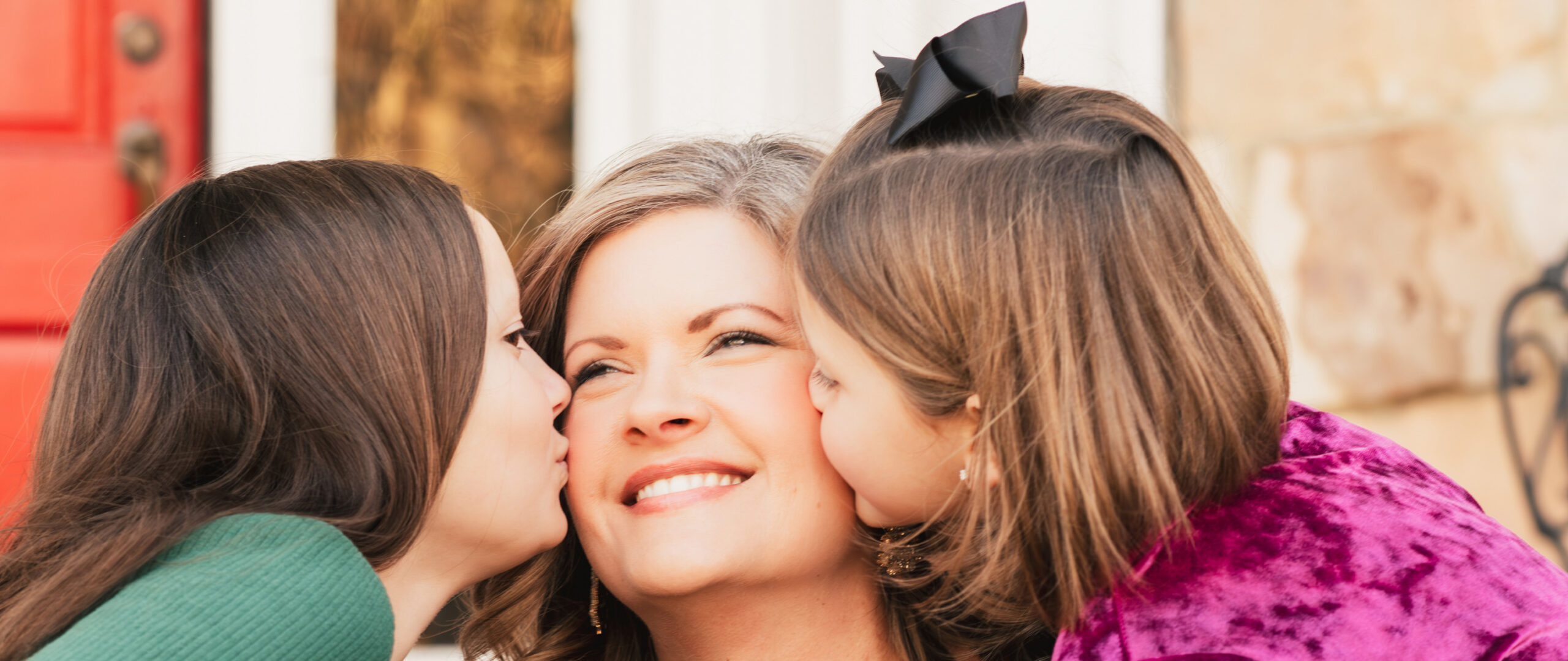 two girls kiss their mother during a family photo shoot