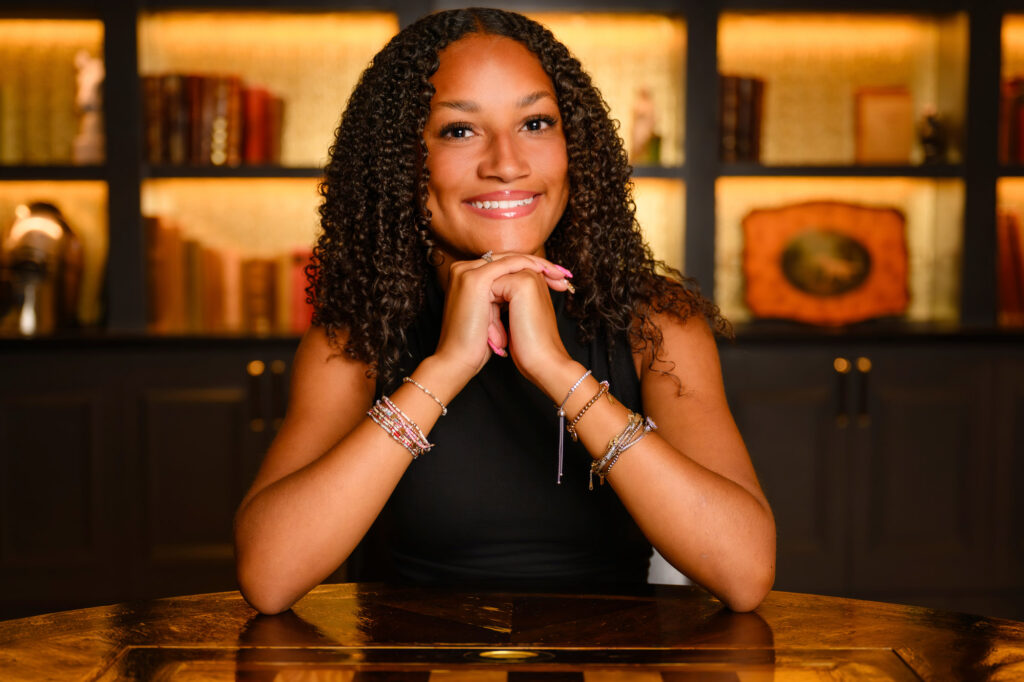 Senior portrait at the Read House Chattanooga — smiling high school senior leaning on gold table with backlit library shelves behind her